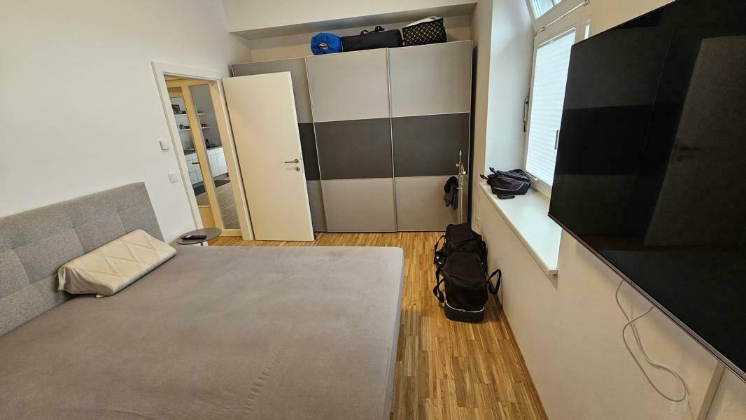 Schlafzimmer mit Doppelbett, großem Schiebetürenschrank, Holzboden und natürlichem Lichteinfall.