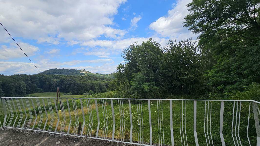 Ausblick von einem Balkon mit Metallgeländer auf eine weite, grüne Hügellandschaft.