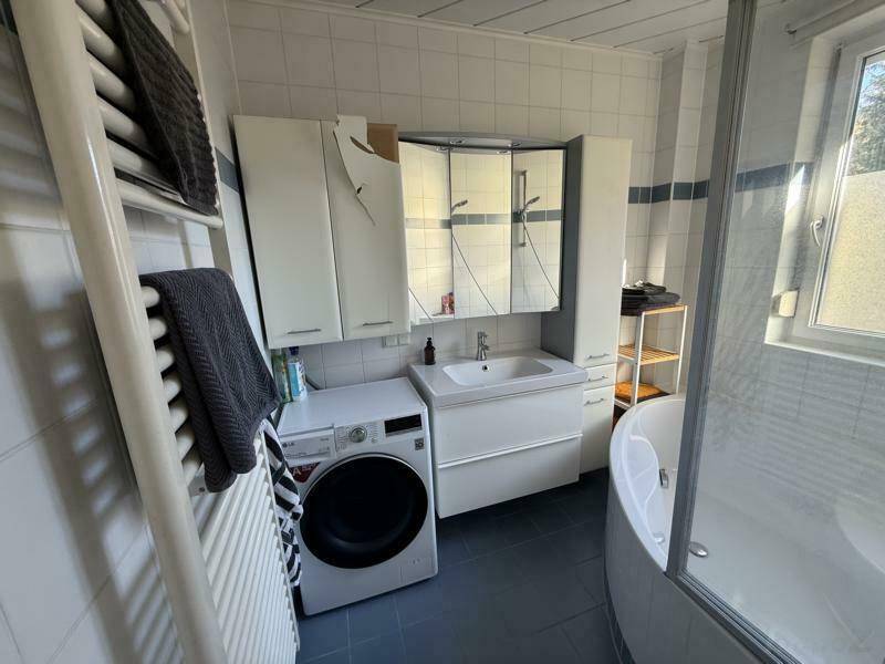 Funktionales Badezimmer mit Waschmaschine, Waschbecken und Dusch-Badewanne, ausgestattet mit einem beheizten Handtuchhalter.