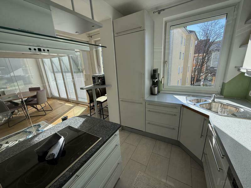 Helle Einbauküche mit Spüle, Kühlschrank und großem Fenster, das einen schönen Ausblick und viel Licht bietet.
