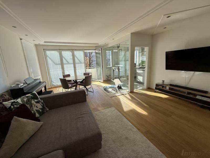 Heller Wohn-Essbereich mit Parkettboden, gemütlichem Sofa und Zugang zu einem Balkon, offen zur Küche.