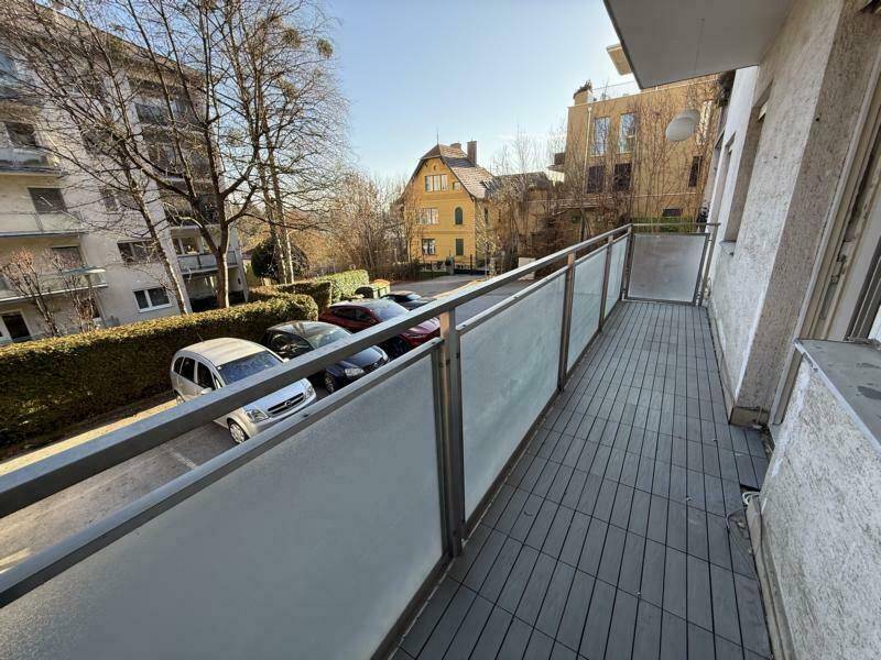 Langer Balkon mit Glasbrüstung und Blick auf die Straße und parkende Autos.