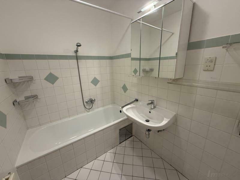 Badezimmer mit Badewanne, Waschbecken und Wandfliesen im 80er-Jahre-Stil.