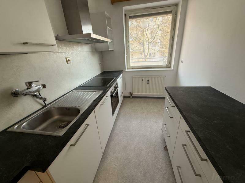 Leere Küche mit weißen Unterschränken, dunkler Arbeitsplatte und Fenster.