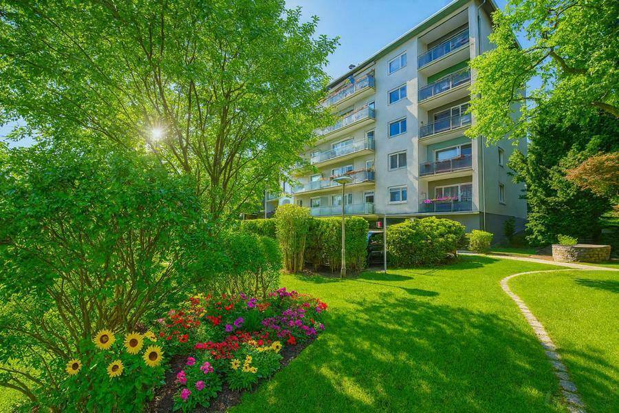 Gepflegte Gartenanlage mit bunten Blumenbeeten und einem Mehrfamilienhaus im Hintergrund.