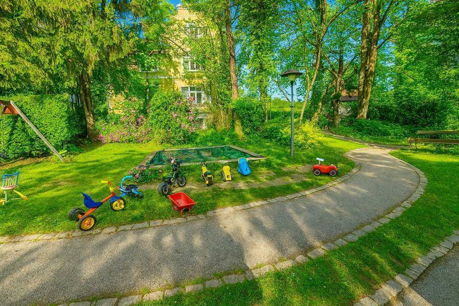 Kinderspielplatz mit Sandkasten und Spielgeräten in einer grünen Gartenanlage.