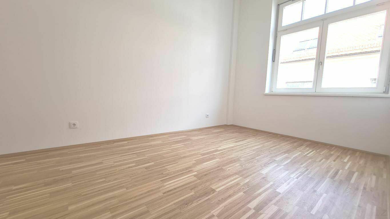 Heller, leerer Raum mit großem Fenster und neuem Parkettboden, ideal für vielfältige Nutzung.