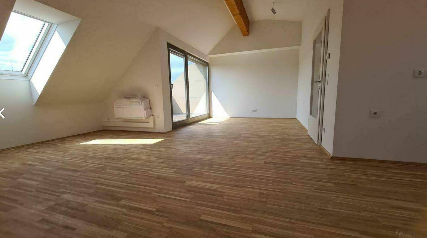 Heller, leerer Wohnbereich im Dachgeschoss mit Holzboden, Dachfenster und Terrassenzugang.