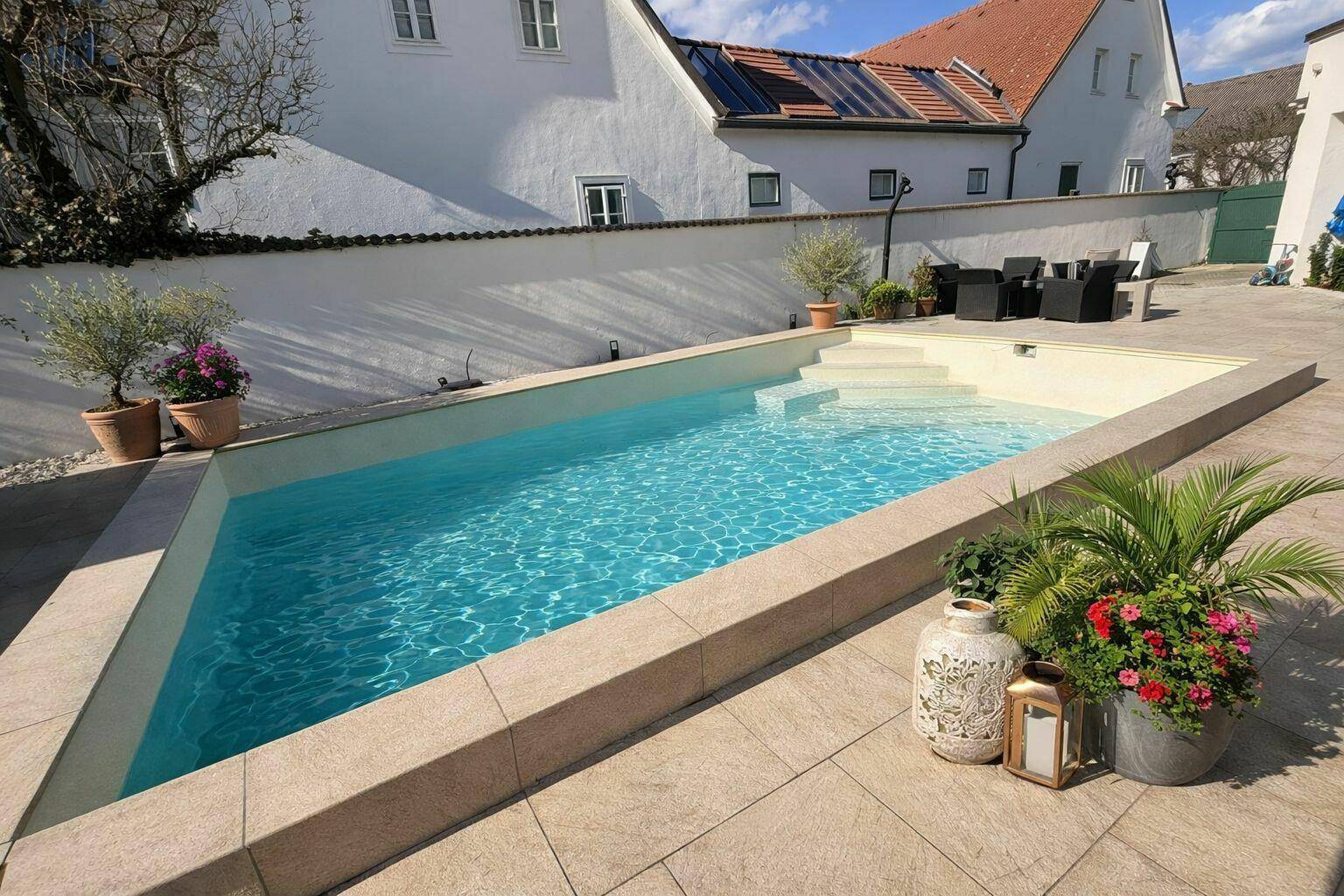 Moderner Poolbereich mit gefliestem Rand, Liegeflächen und mediterranen Pflanzen.
