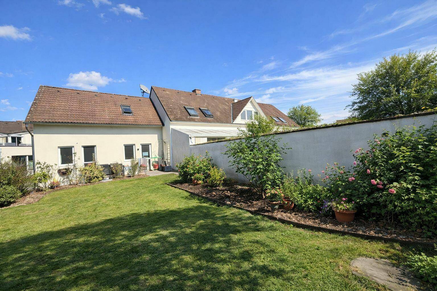Rückansicht des Hauses mit großem Rasenbereich und gepflegten Sträuchern unter blauem Himmel.