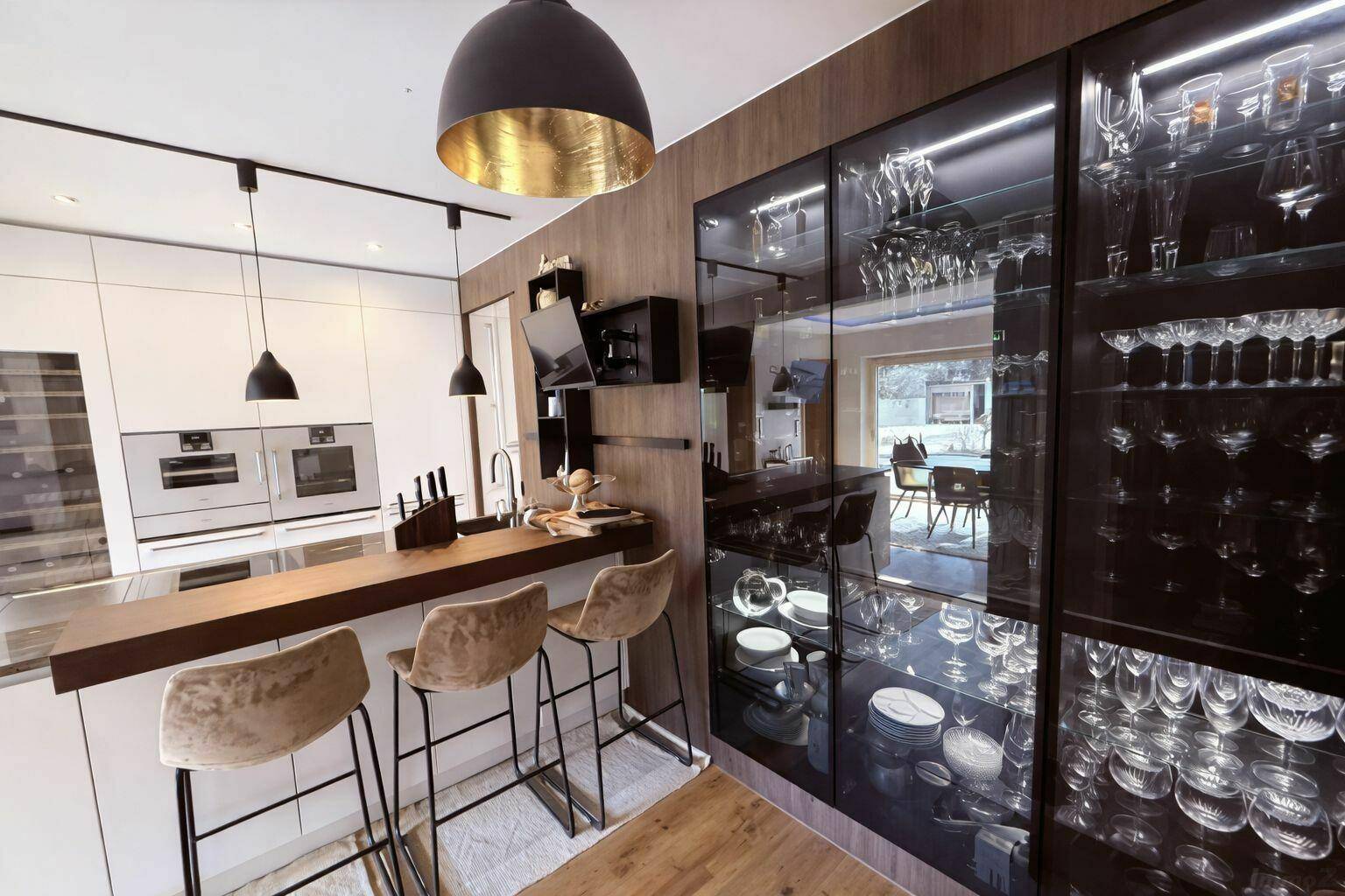 Elegante moderne Küche mit Kochinsel, integrierten Geräten und beleuchteten Glasvitrinen für Geschirr.