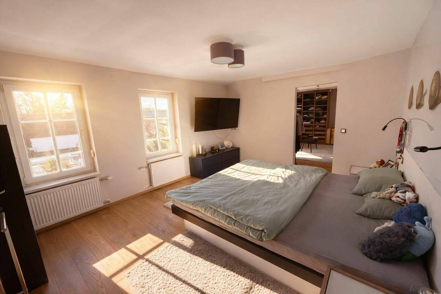 Sonniges Schlafzimmer mit Holzboden, großem Bett und Zugang zum begehbaren Kleiderschrank.