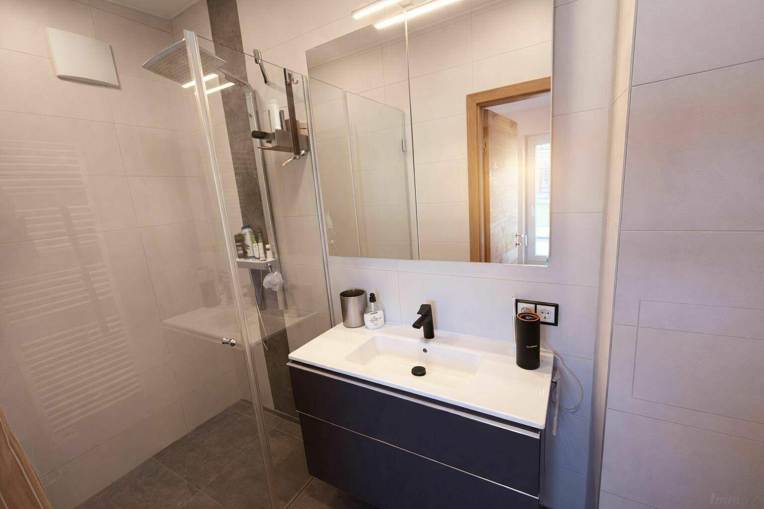 Modernes Badezimmer im Dachgeschoss mit Dusche, Waschtisch und Spiegel.