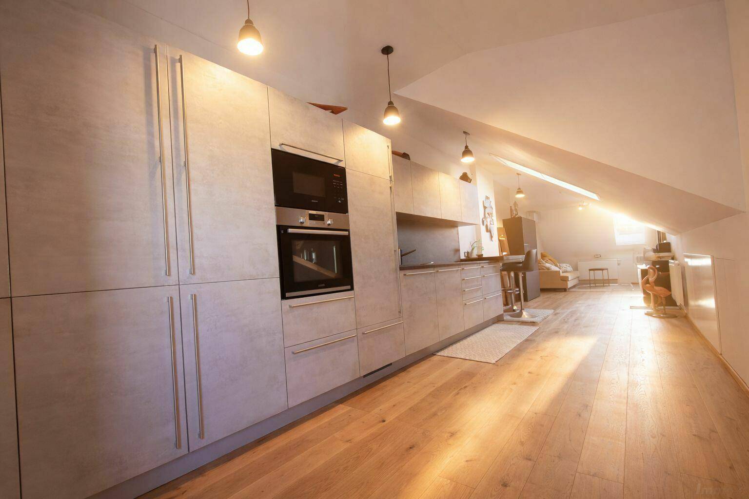 Moderne Küche im Dachgeschoss mit Schrägdach, Einbaugeräten und Holzboden.