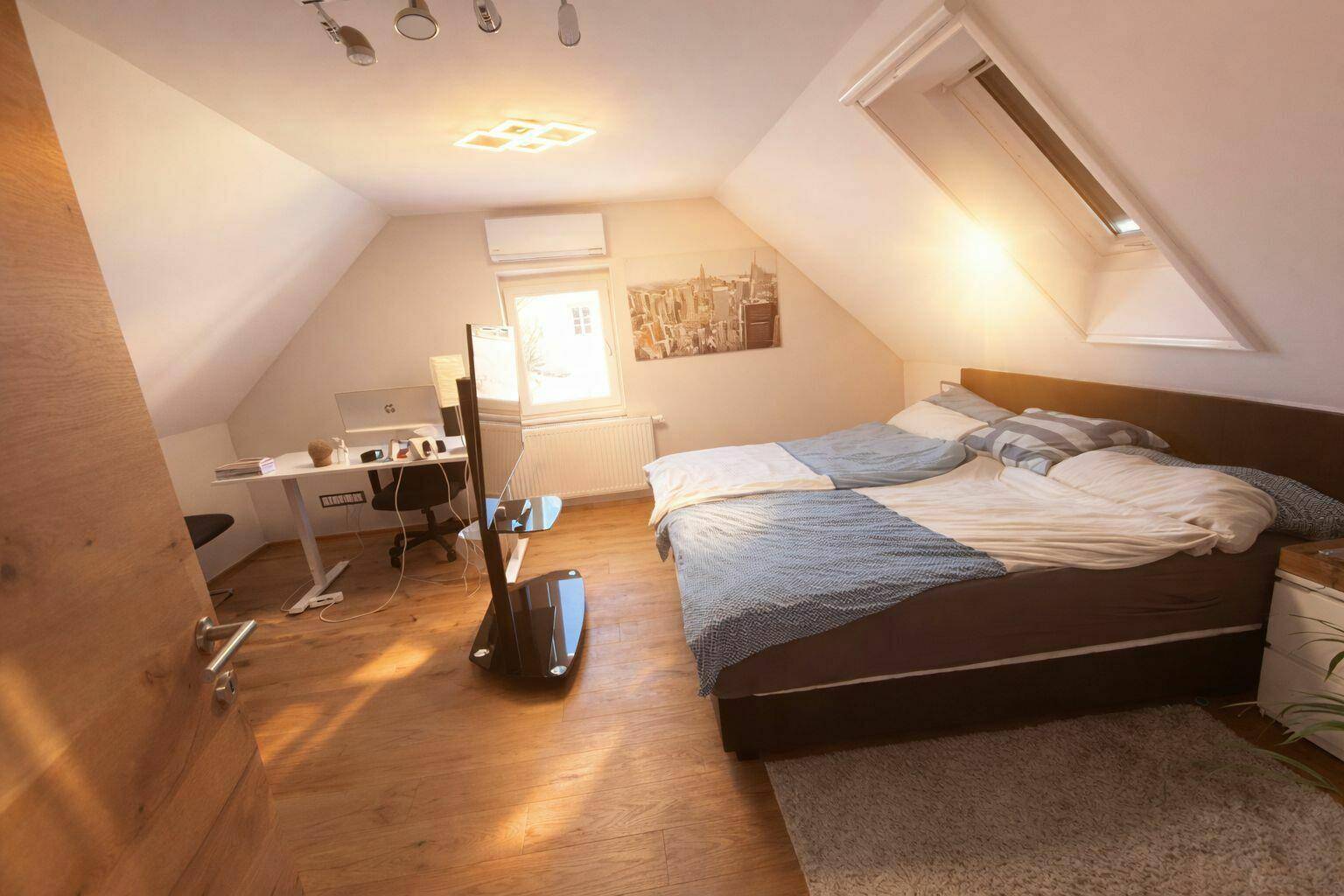 Sonniges Schlafzimmer im Dachgeschoss mit Doppelbett, Schreibtisch und Dachfenster.