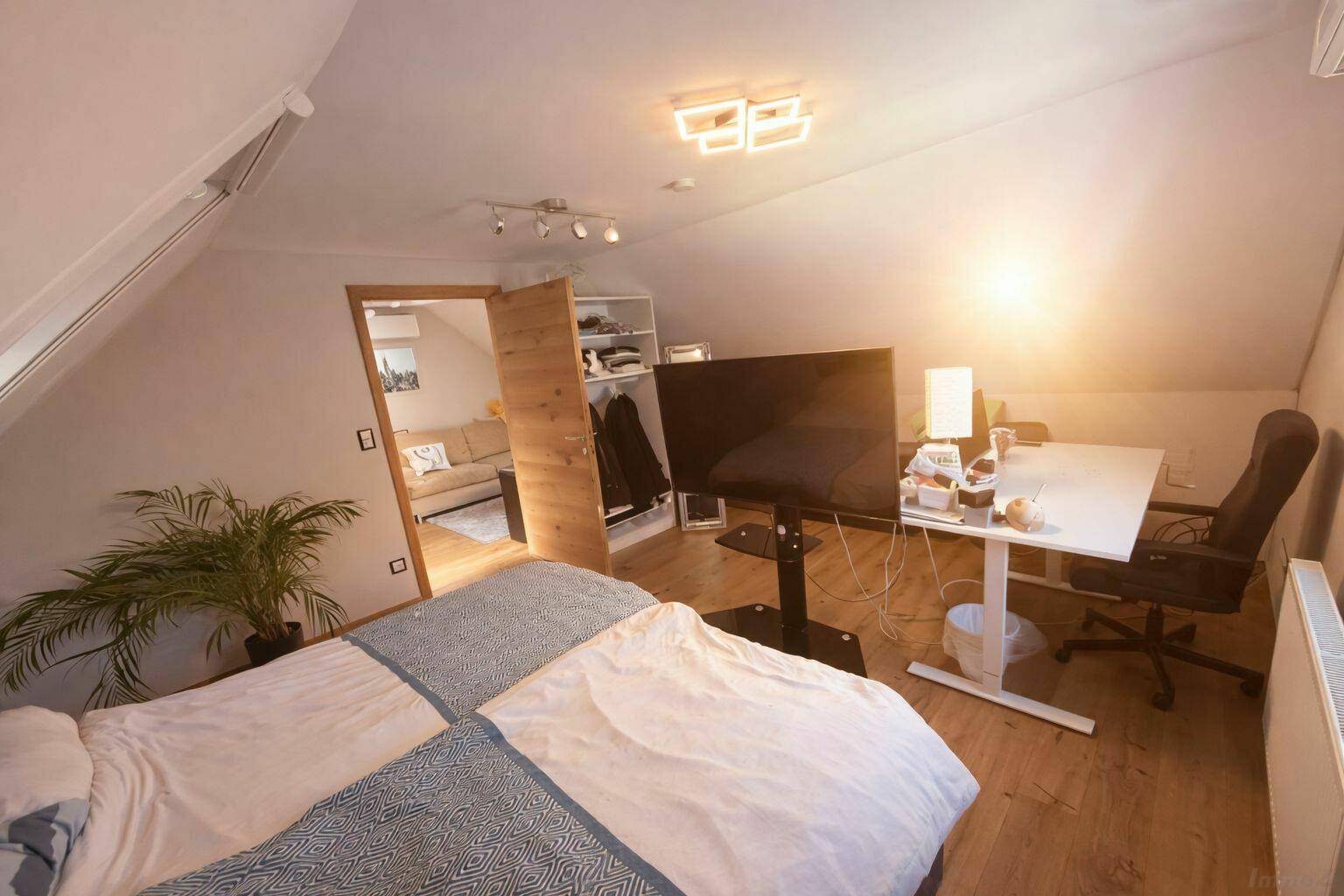Helles Schlafzimmer im Dachgeschoss mit Doppelbett, Schreibtisch und Dachfenster.