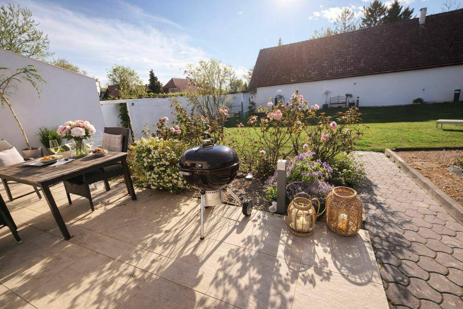 Sonniger Terrassenbereich mit Grill, Gartenmöbeln und Blick auf den Rosengarten.