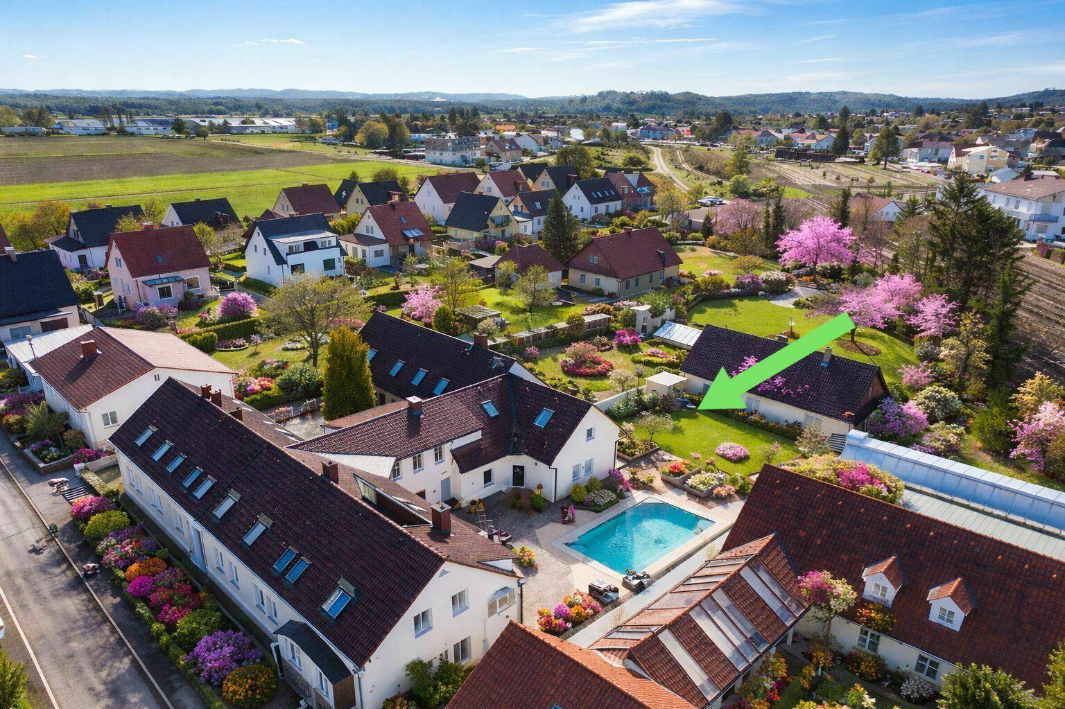 Luftaufnahme des Anwesens mit Pool und umliegender Wohnsiedlung in grüner Umgebung.