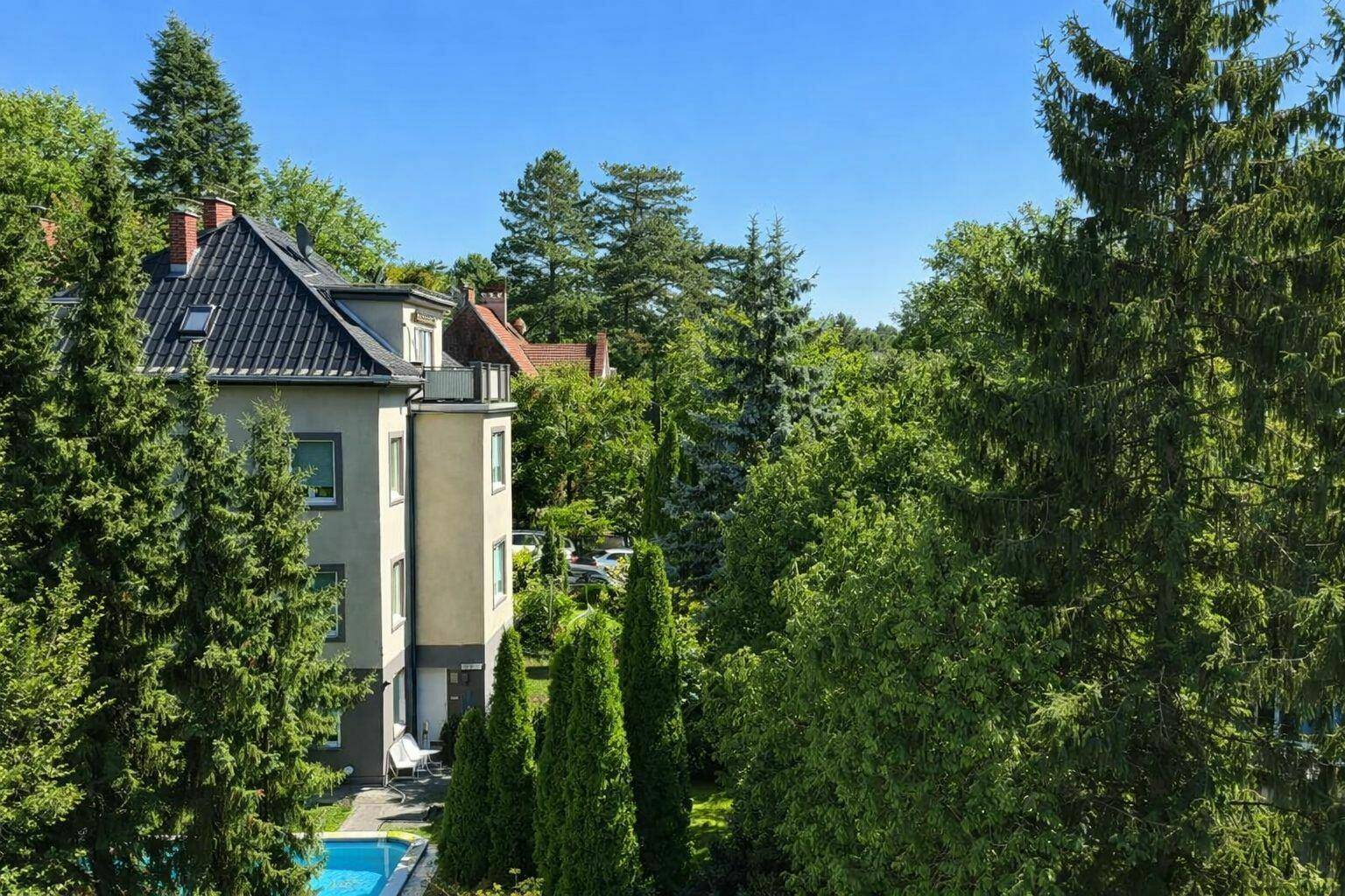 Attraktives Gebäude umgeben von üppigem Grün und hohen Bäumen, mit einem privaten Pool im Gartenbereich.