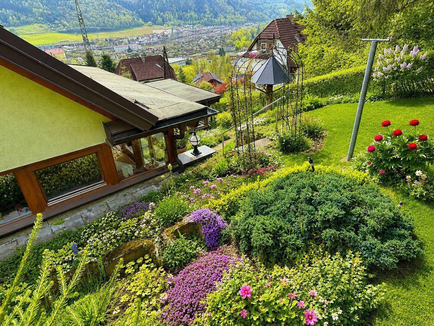 Farbenfroher Ziergarten mit vielfältigen Pflanzen, Blumen und einem malerischen Blick auf die Umgebung.