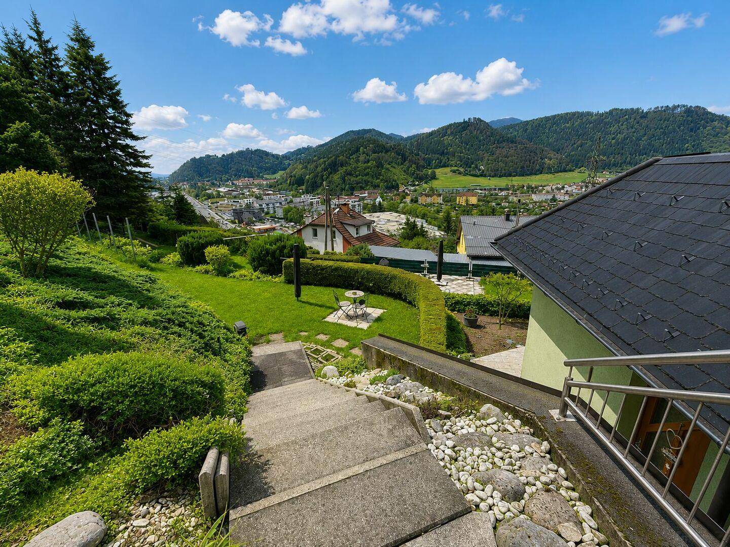 Außentreppe führt durch einen gepflegten Garten mit Steinen und bietet einen weiten Blick ins Tal.