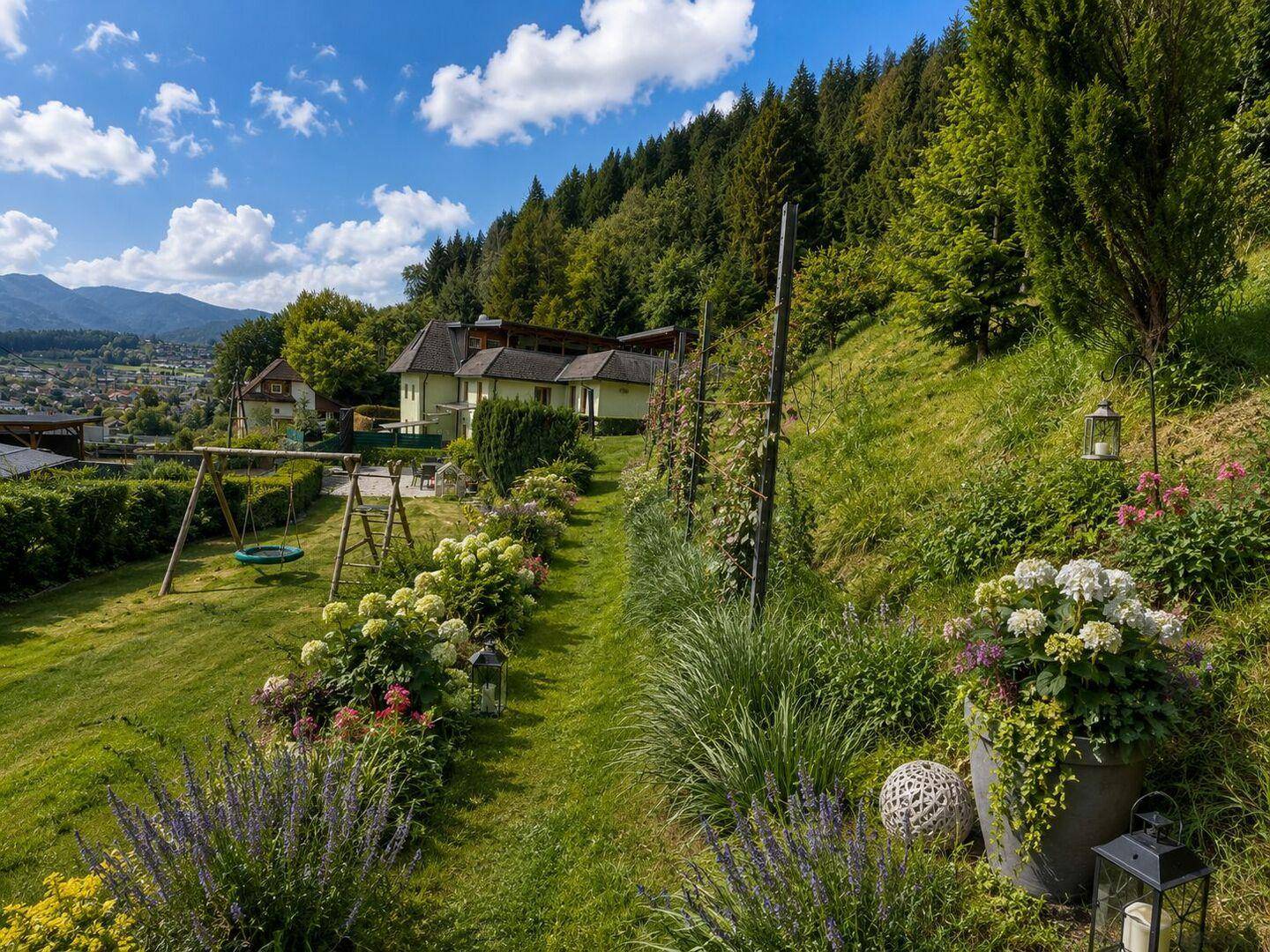 Weitläufiger Garten mit Schaukel, Blumenbeeten und einem malerischen Blick auf die Umgebung.