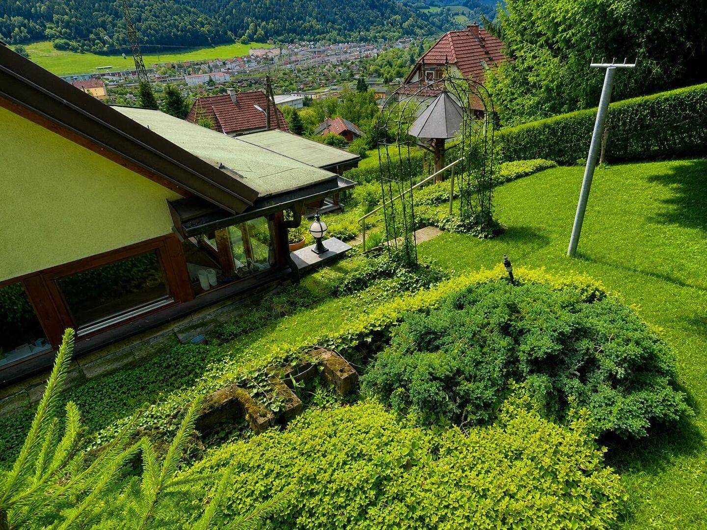Gepflegter Gartenbereich mit Sträuchern, Rasen und einem weiten Blick auf die Stadt und die Berge.