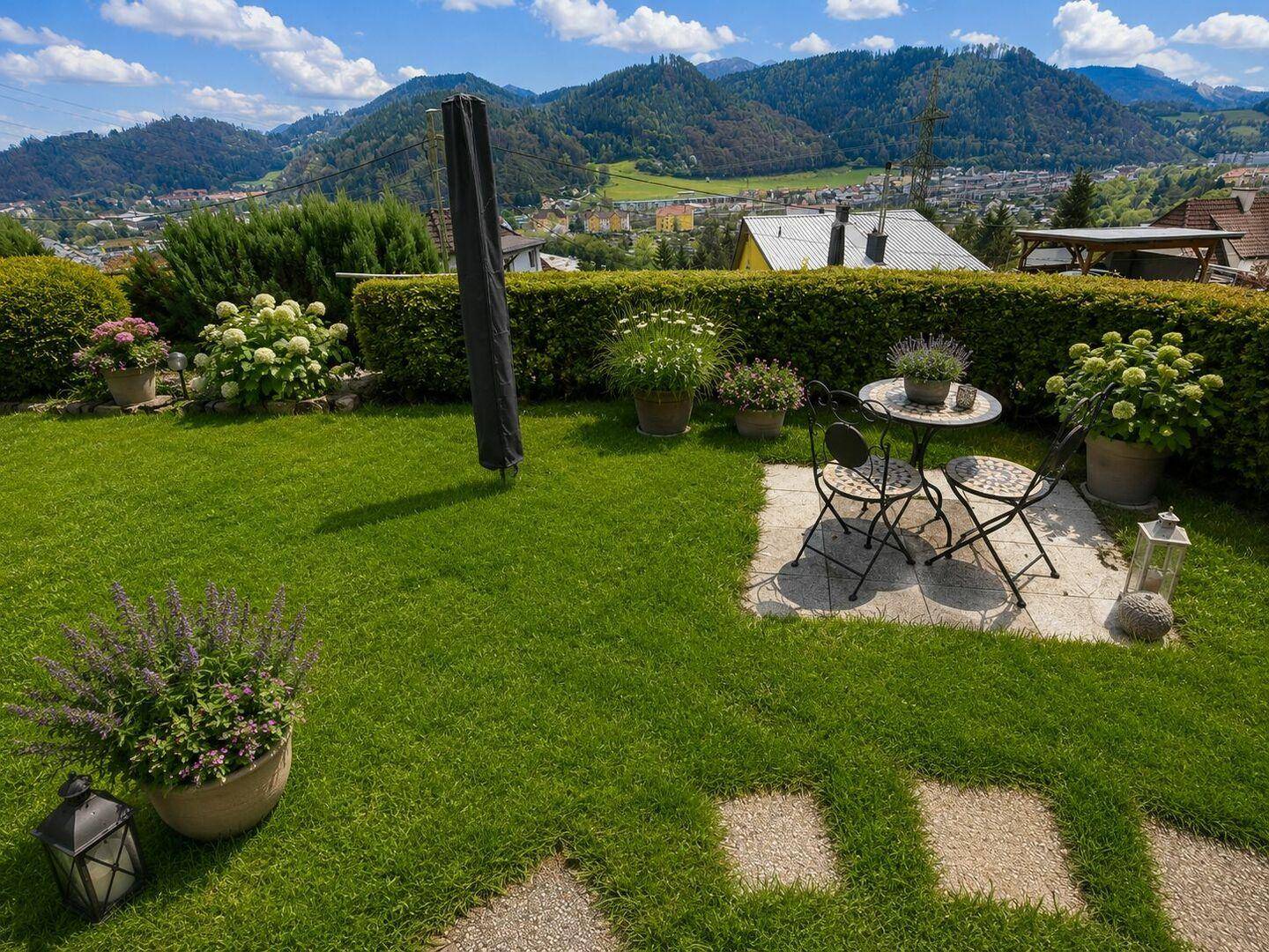 Sonniger Garten mit Rasenfläche, kleiner Sitzecke und weitem Blick auf die umliegende Landschaft.