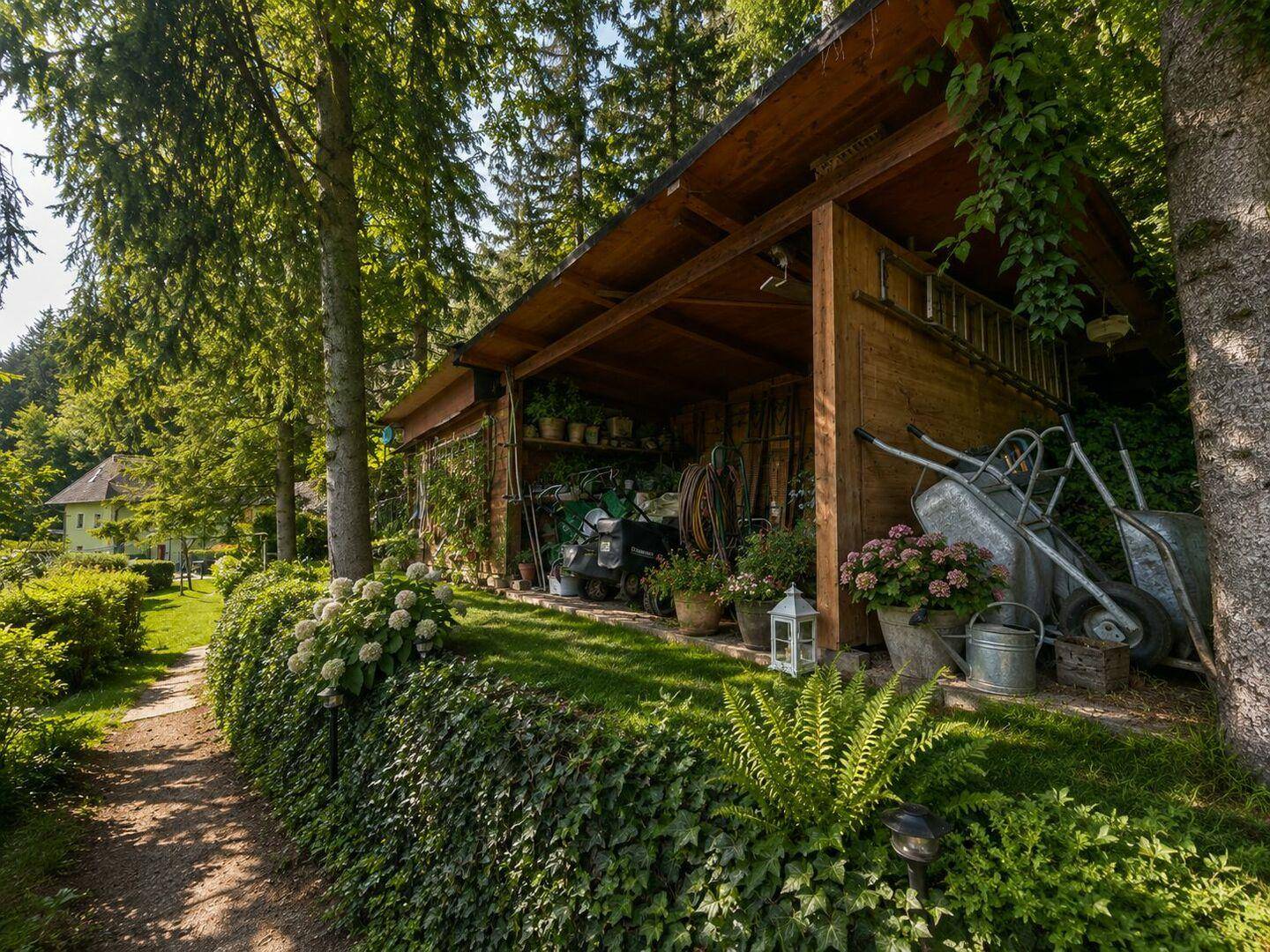 Rustikaler Holzschuppen im Garten, umgeben von üppigem Grün und einem schattigen Pfad.