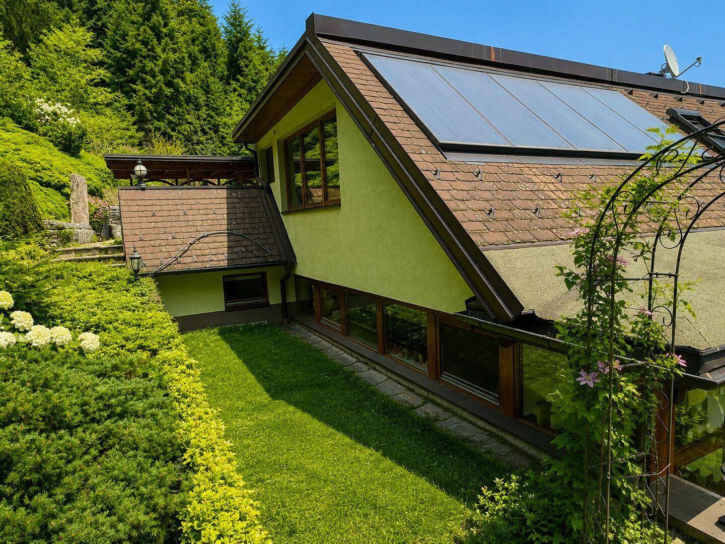 Ansicht des Hauses mit Solarpaneelen auf dem Dach und einem gepflegten Gartenbereich mit Blumen.