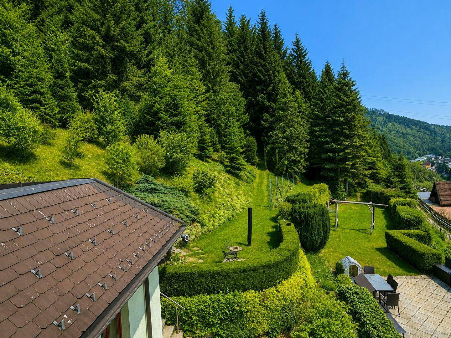 Weitläufiger Gartenbereich mit gepflegtem Rasen, Hecken und einem kleinen Sitzbereich mit Bergblick.