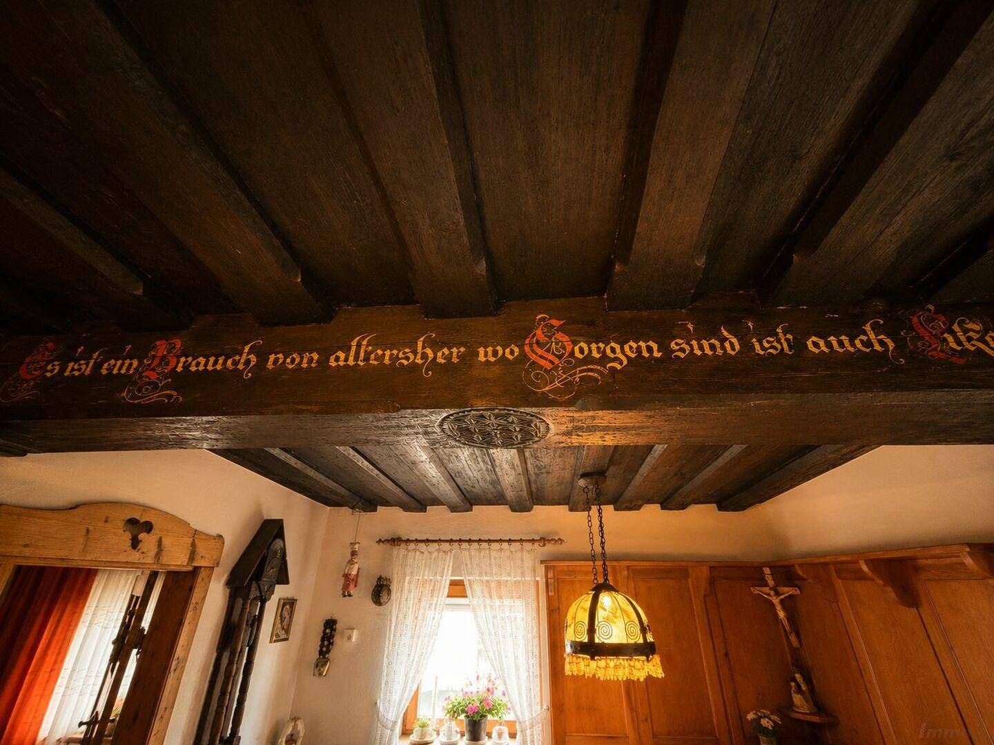 Detailaufnahme der Holzbalkendecke mit traditioneller Inschrift und rustikaler Beleuchtung.