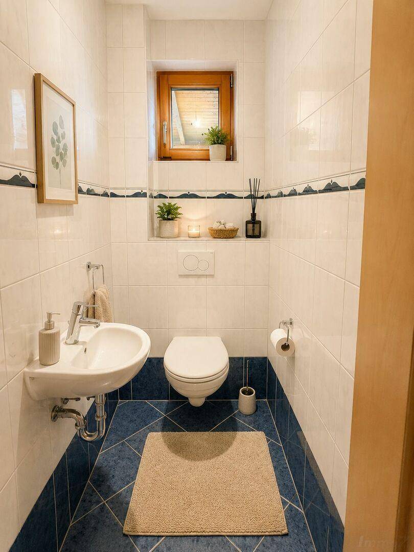 Helles Gäste-WC mit blauen Fliesen, Wand-WC und kleinem Waschbecken.