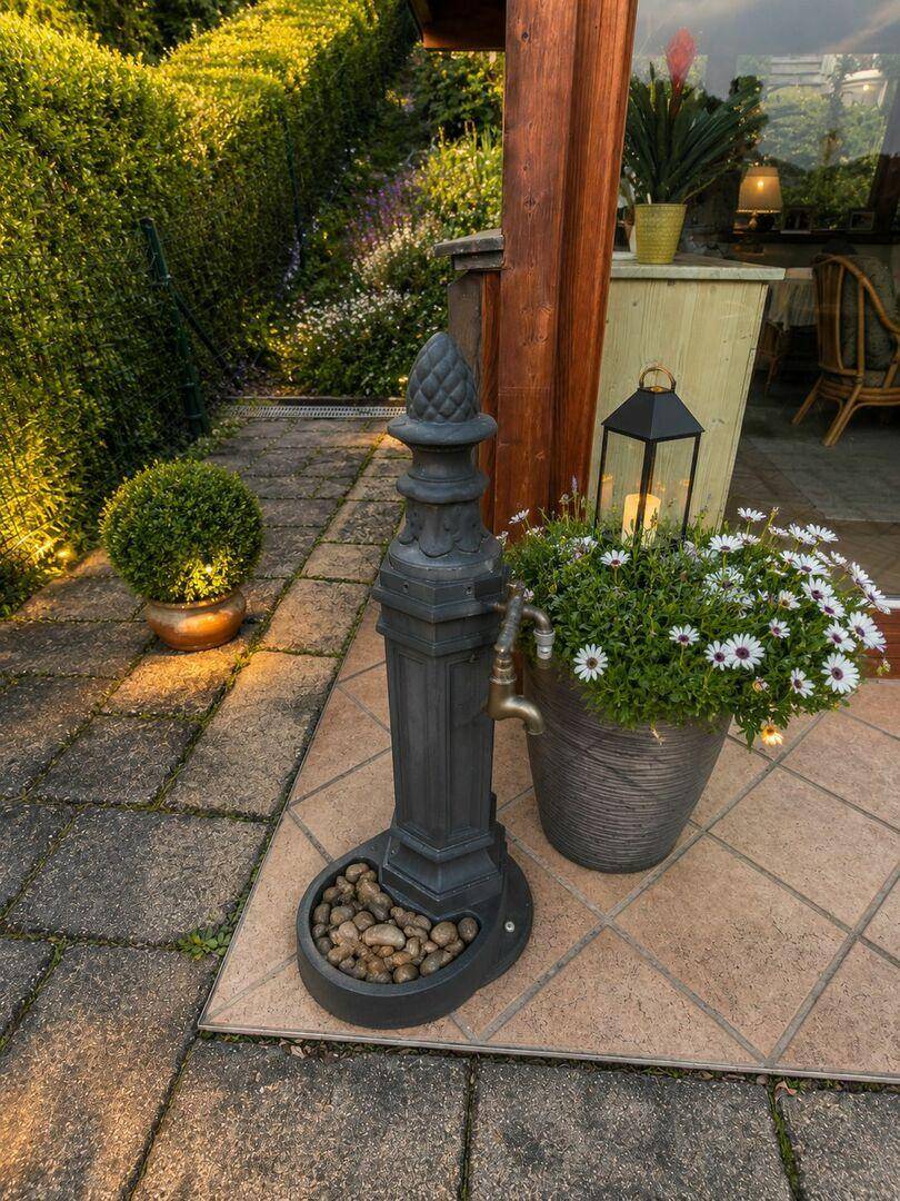 Charmante Terrasse mit dekorativem Wasserhahn, Blumen und Fliesenboden.