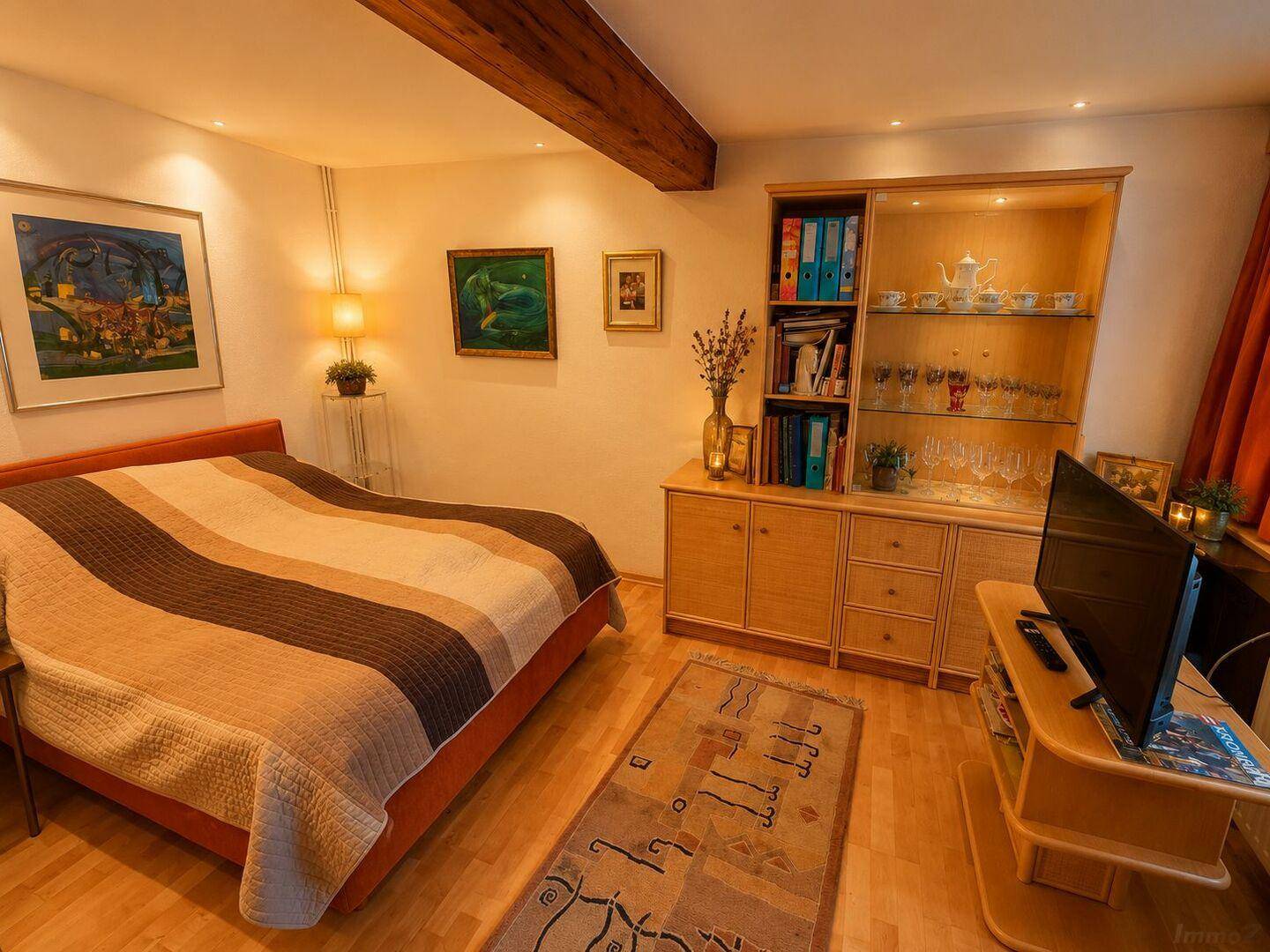 Komfortables Schlafzimmer mit Holzboden, Vitrine und sichtbarem Deckenbalken.