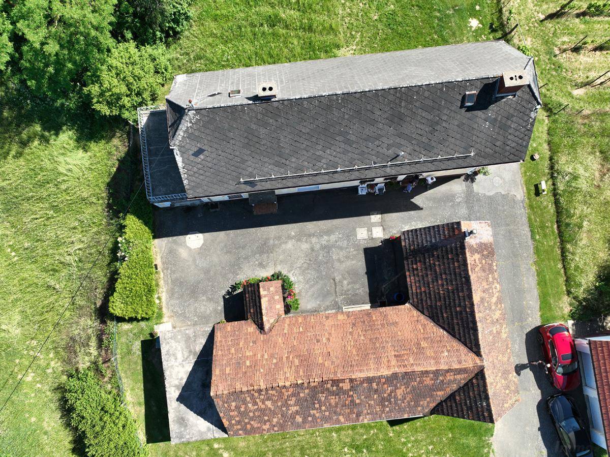 Draufsicht auf das Anwesen mit verschiedenen Dächern und einem gepflasterten Hofbereich.