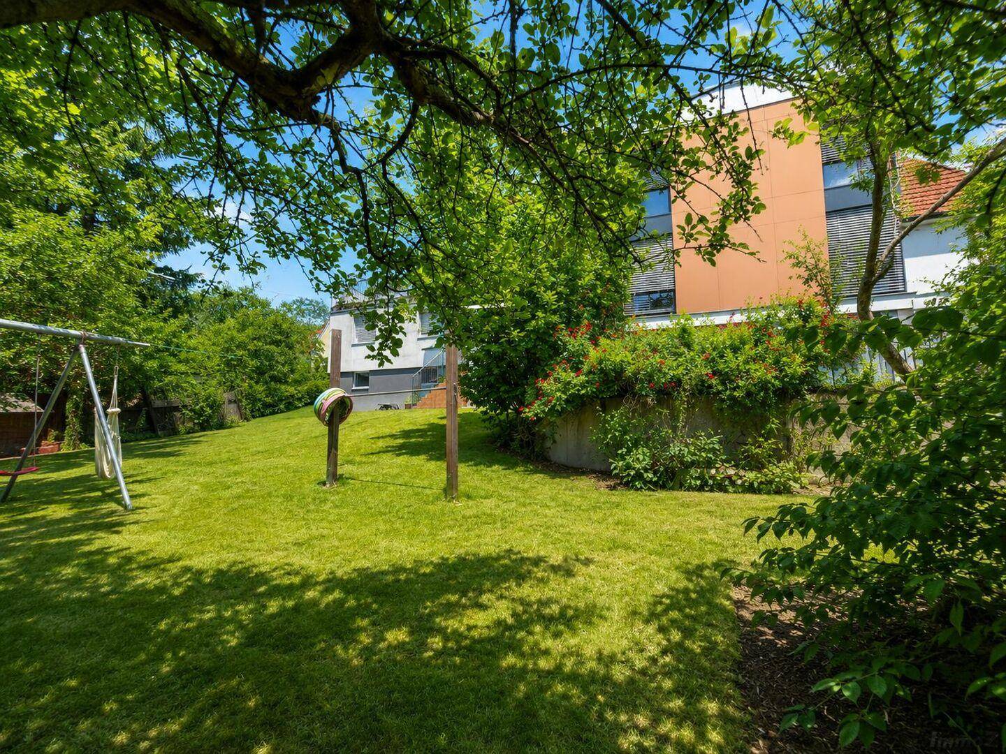 Weitläufiger Garten mit Spielgeräten und Blick auf das moderne Wohnhaus.