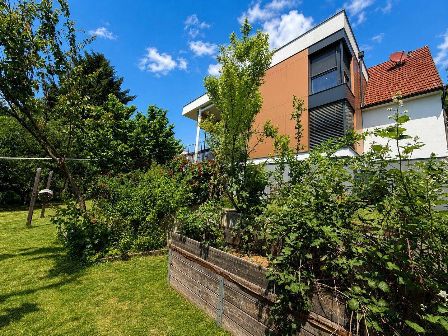 Modernes Wohnhaus umgeben von einem grünen Garten mit Hochbeeten und Sträuchern.