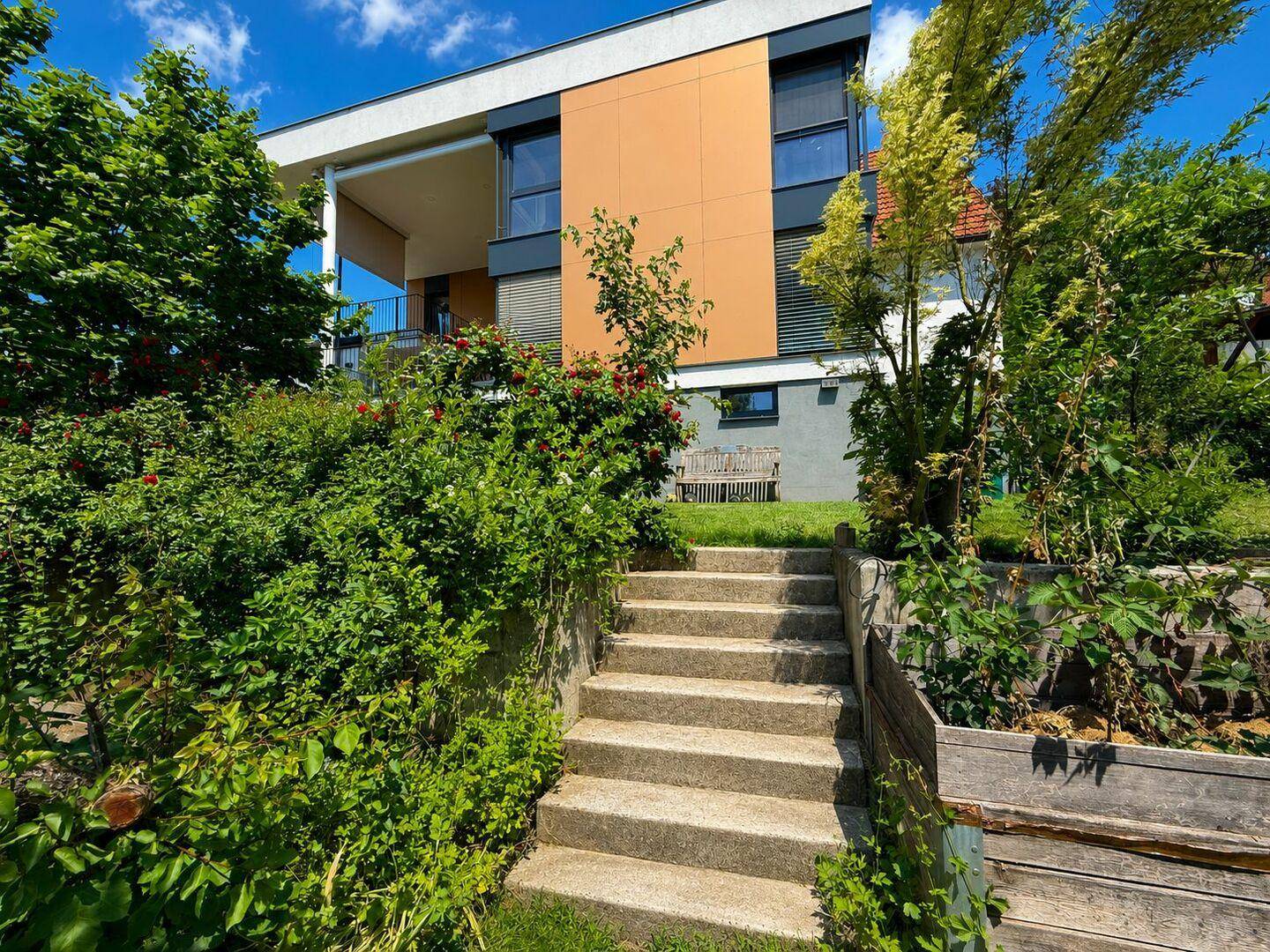Modernes Haus mit terrassiertem Garten und Treppenaufgang im Grünen.