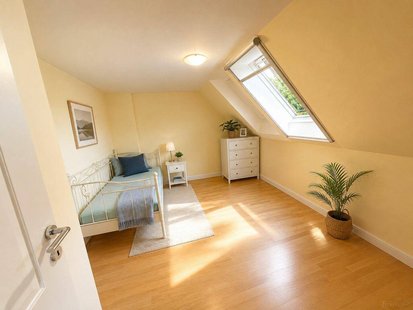 Helles Schlafzimmer im Dachgeschoss mit Holzboden und einem großen Dachfenster.