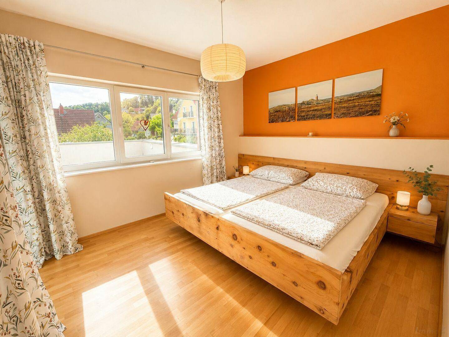 Helles Schlafzimmer mit Holzbett, orangefarbener Akzentwand und großem Fenster.