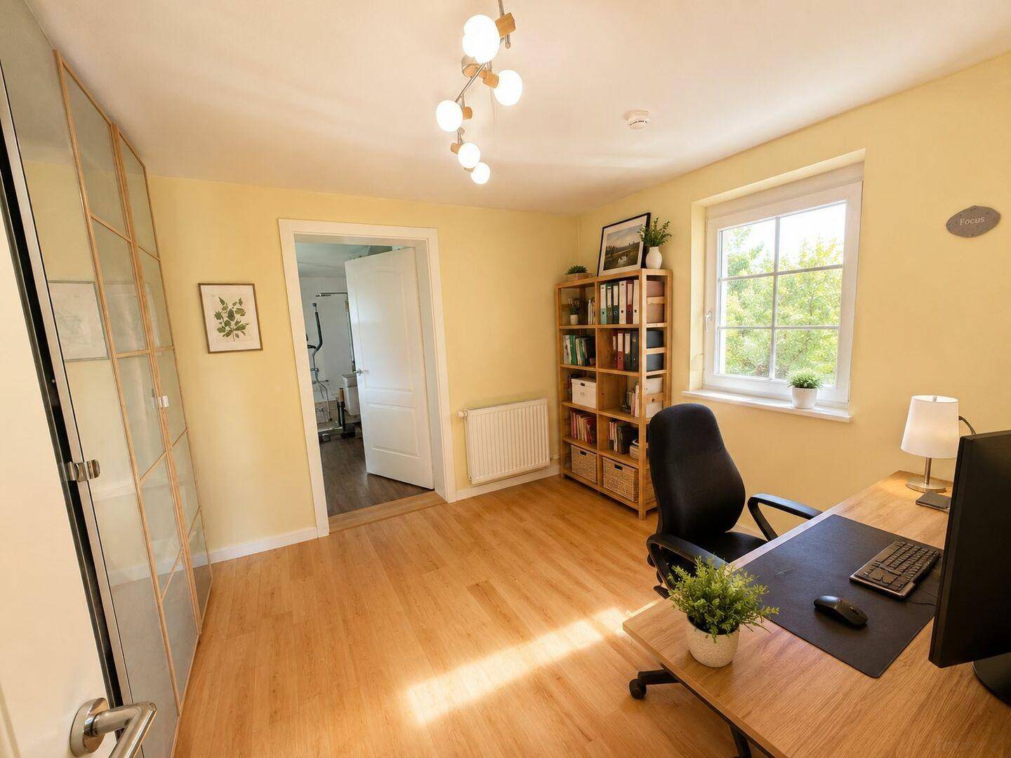 Helles Arbeitszimmer mit Holzboden, Schreibtisch und Fenster mit Blick ins Grüne.