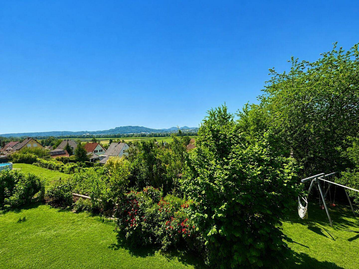 Weitläufiger Gartenbereich mit Schaukel und Blick auf die umliegende Landschaft.