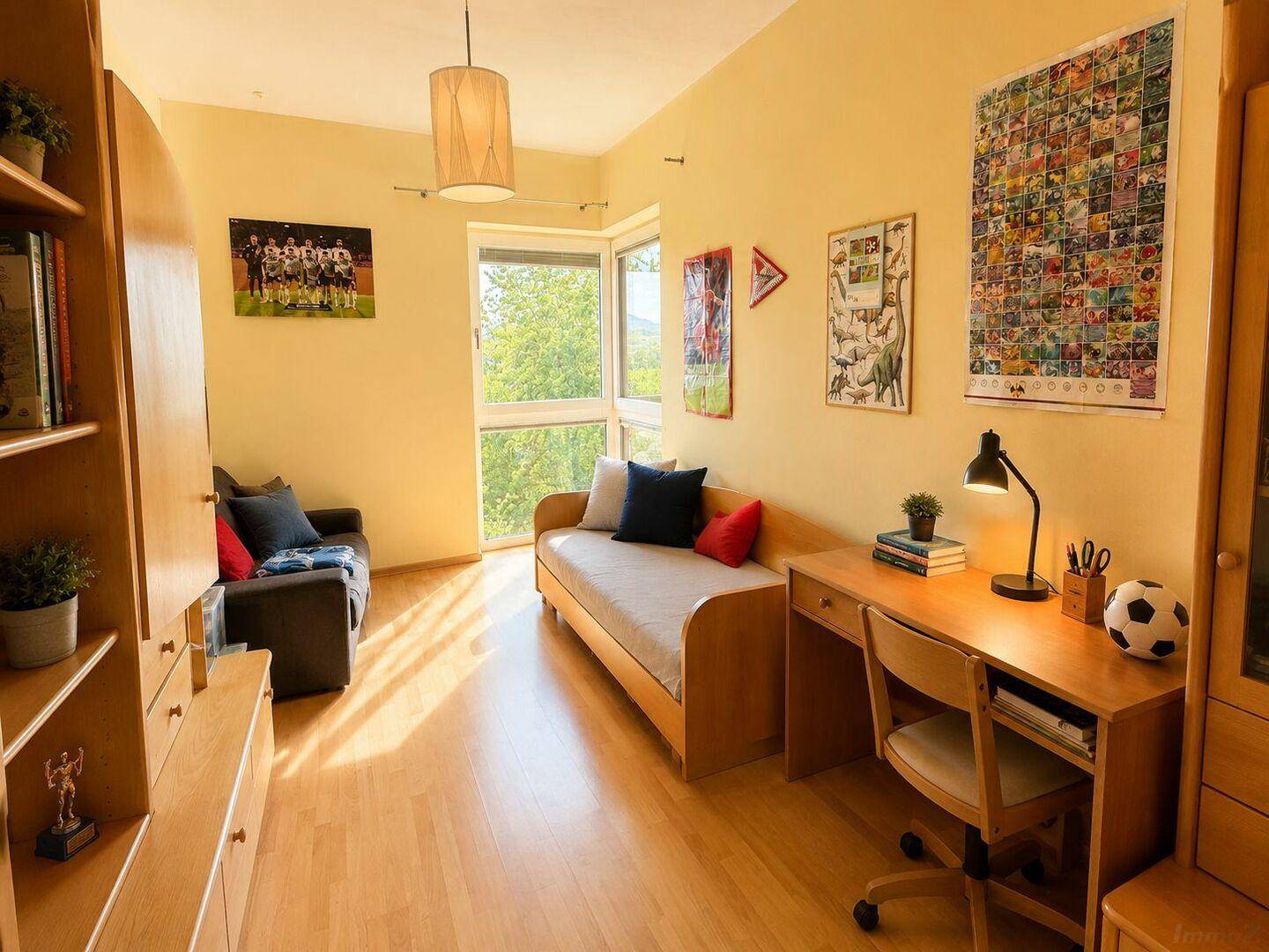 Kinderzimmer mit Holzboden, Schreibtisch und einem großen Fenster mit Blick ins Grüne.