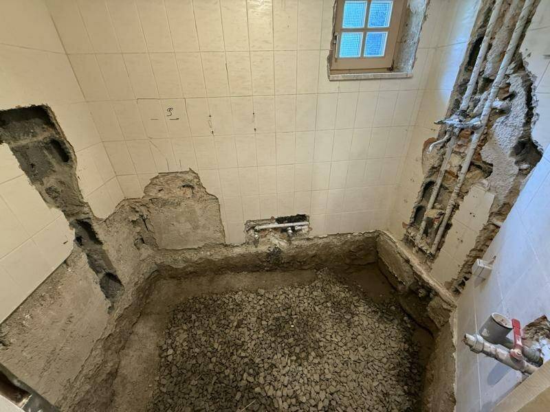 Badezimmer im Rohbauzustand mit freigelegten Wänden und Fliesenresten, bereit zur Renovierung.