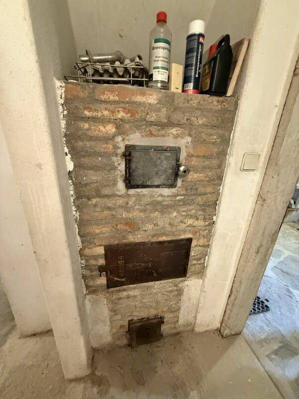 Detailansicht eines gemauerten Ofens mit Metalltüren im Kellerbereich, traditionelle Heizquelle.