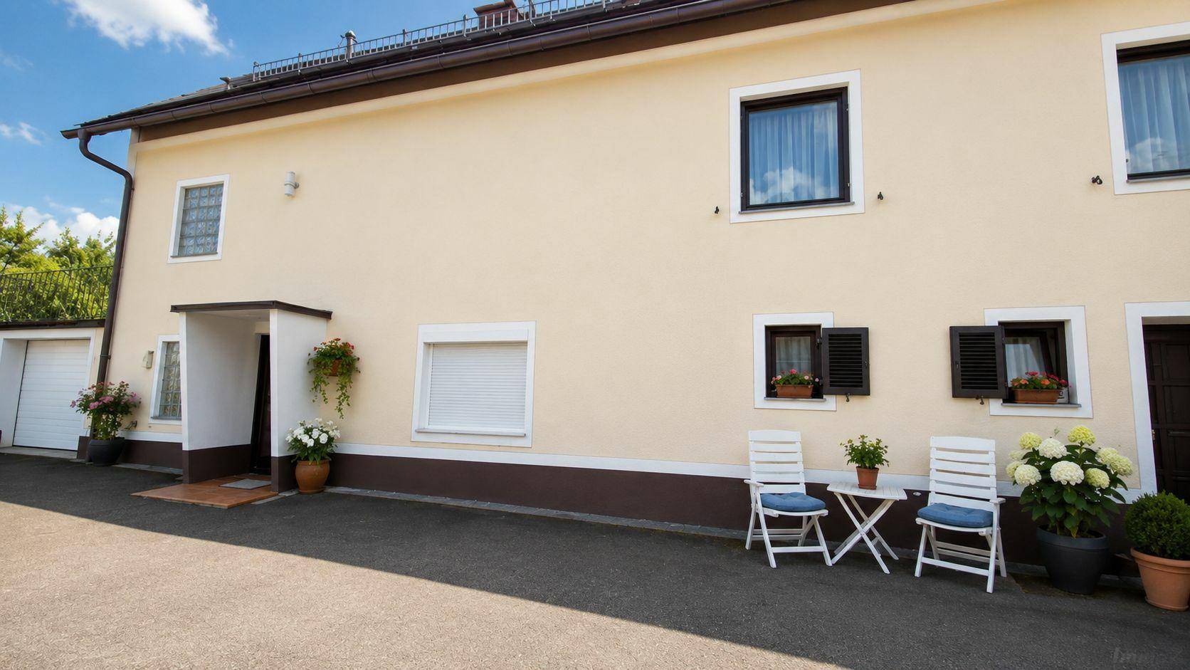 Vorderseite des Hauses mit gepflastertem Bereich und kleiner Sitzgelegenheit im Freien.