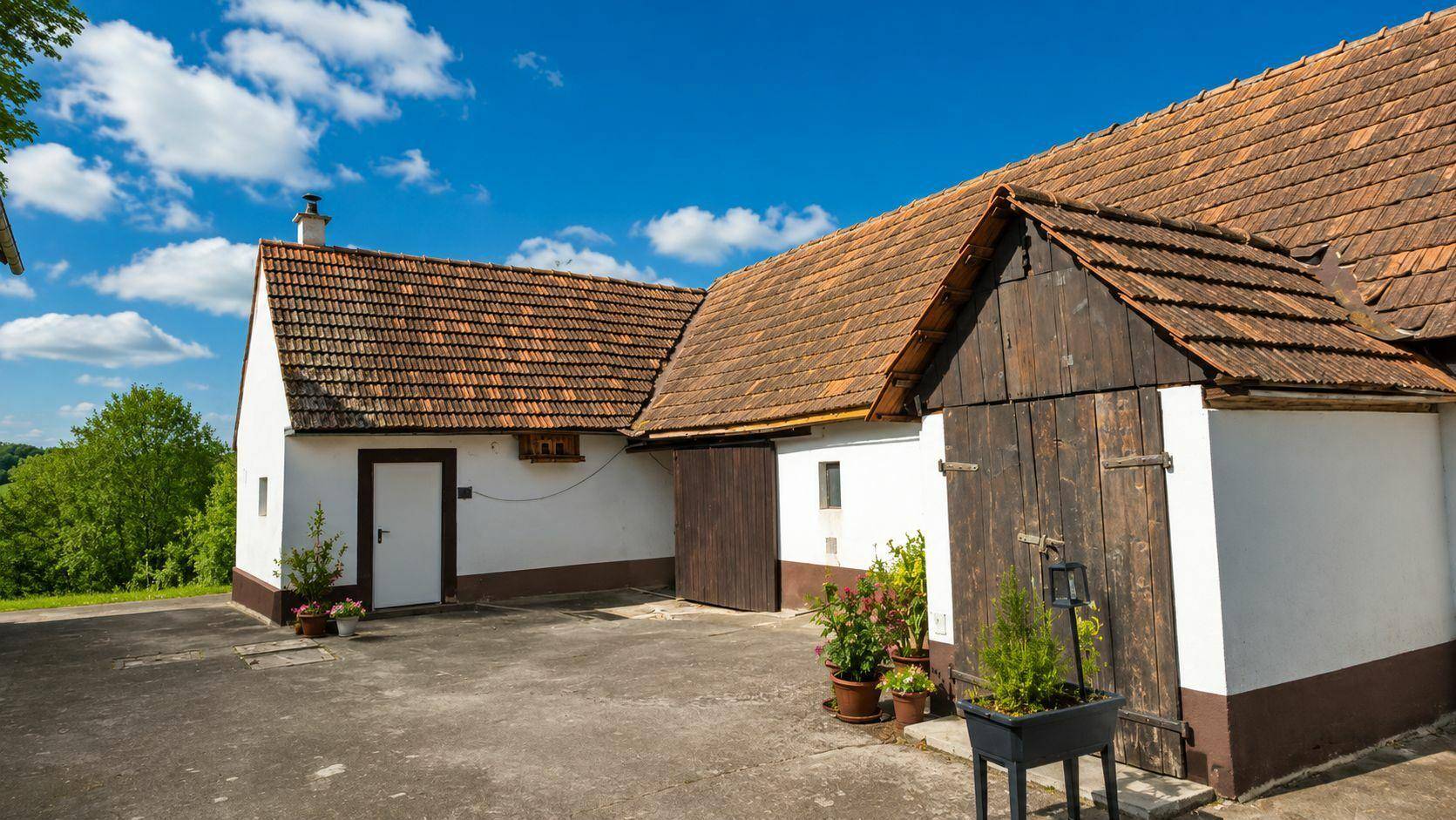 Rustikales Nebengebäude mit Holztüren und Ziegeldach in ländlicher Umgebung.