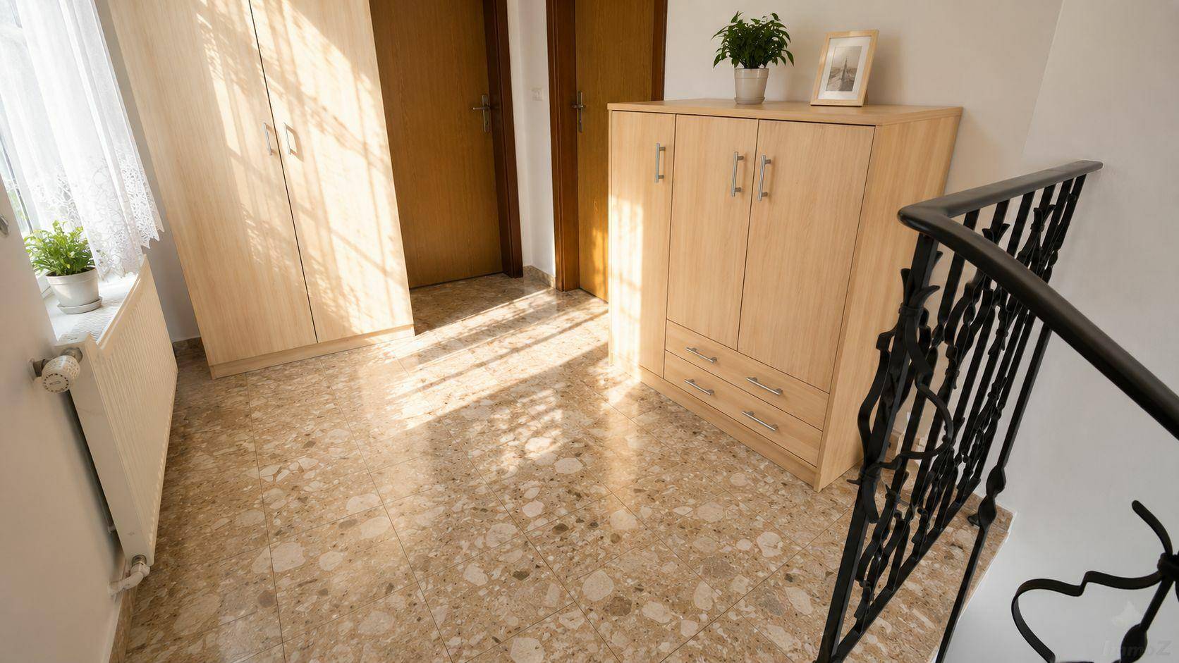 Heller Flur mit Terrazzoboden, Holzschränken und schmiedeeisernem Treppengeländer.