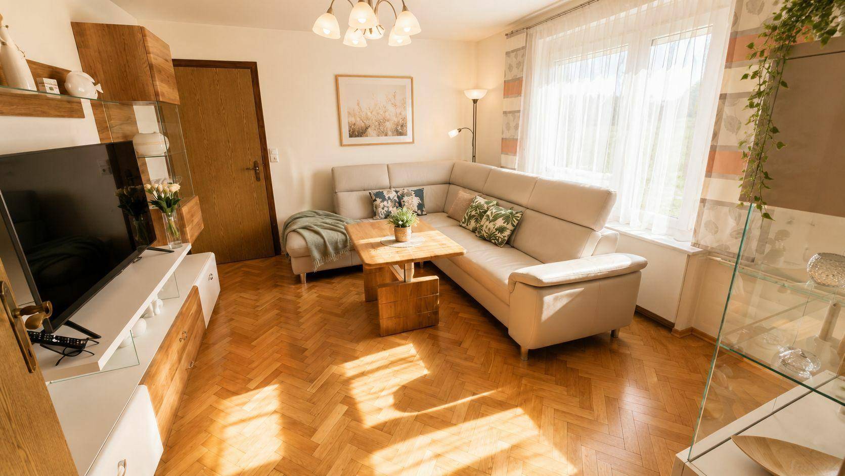 Gemütliches Wohnzimmer mit Fischgrätparkett, Ecksofa und viel natürlichem Licht.
